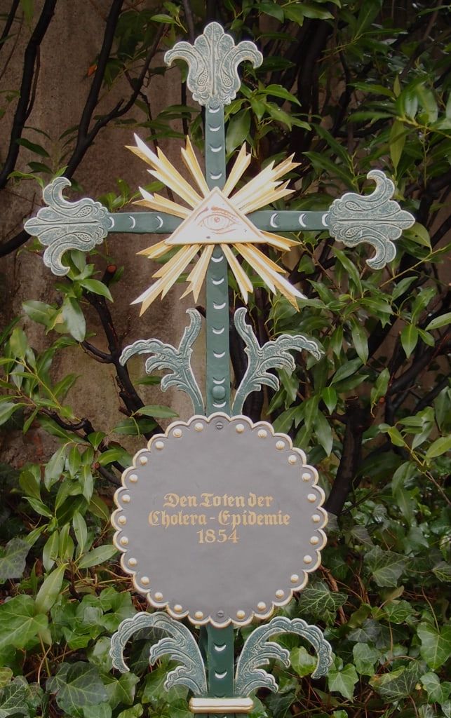 Ornate green memorial cross with a radiant halo and an inscription to those who died in the 1854 cholera epidemic at Haidhausen Cemetery